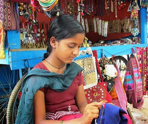 A young girl doing embroidery on a bag for selling it at her stall in Hampi, Karnataka 
